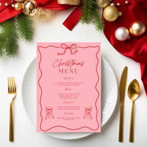 May include: A pink Christmas menu card with a red ribbon and a red border. The menu includes starters, main course, dessert, and drinks. The text reads "Christmas Menu".