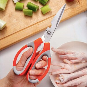 May include: A pair of red and gray kitchen shears with a bottle opener and a serrated blade. The shears are being held by a hand and are positioned over a white bowl with chicken feet.