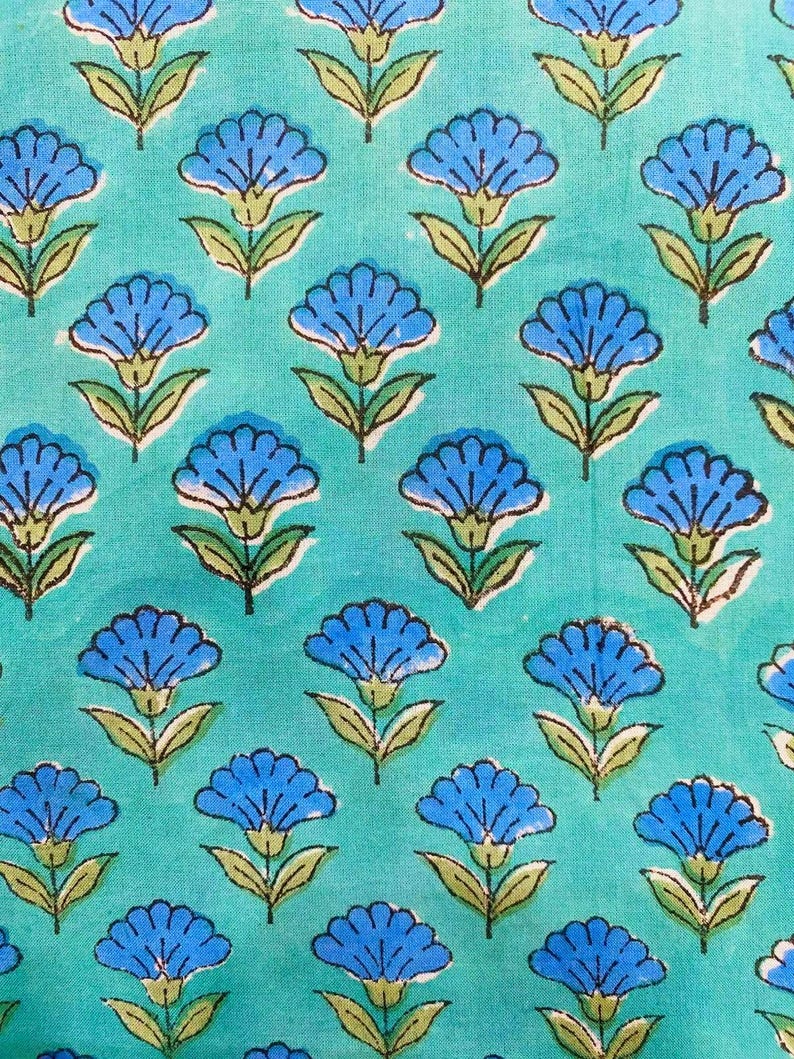 Hand block printed cotton fabric featuring blue floral buta motifs on an aqua turquoise background, handmade in Jaipur, India, perfect for dresses, quilting, sewing, and home décor projects.