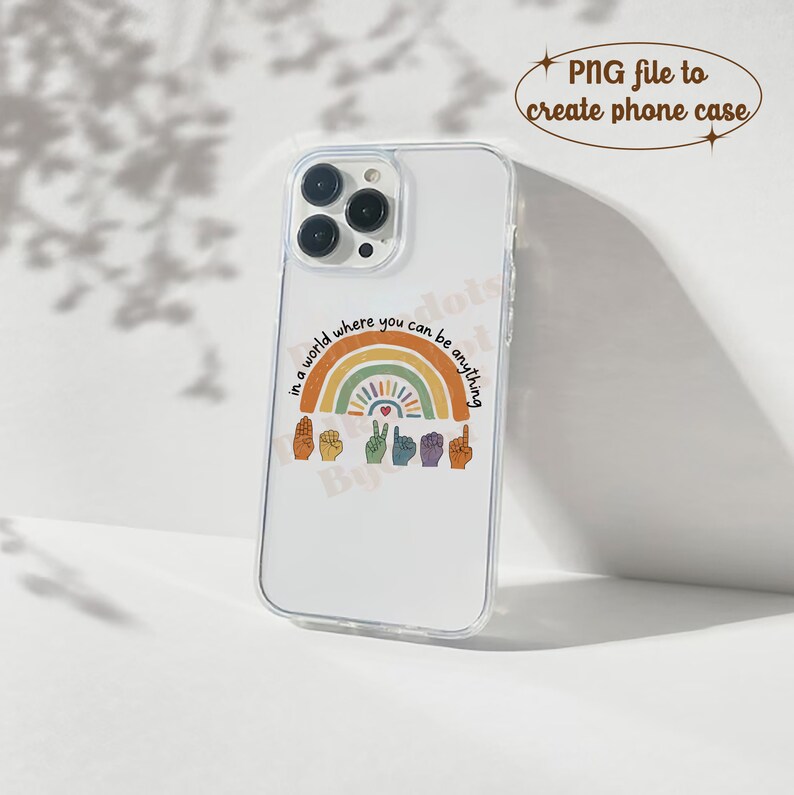 Peut inclure: Coque de t&eacute;l&eacute;phone transparente avec un motif arc-en-ciel color&eacute; et le texte "in a world where you can be anything". Le design comprend des gestes de la main et un c&oelig;ur. Con&ccedil;u pour smartphone.