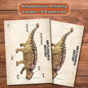 Puede incluir: Dos páginas educativas tituladas "Anatomía de Ankylosaurus" para niños de 5 a 8 años, con una ilustración de dinosaurio y etiquetas como "Cola de maza" y "Placas de armadura". Las páginas están sobre un fondo de madera.