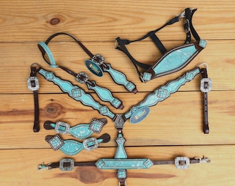 May include: A turquoise and brown leather horse tack set with rhinestones. The set includes a headstall, breast collar, reins, and two sets of bit straps.