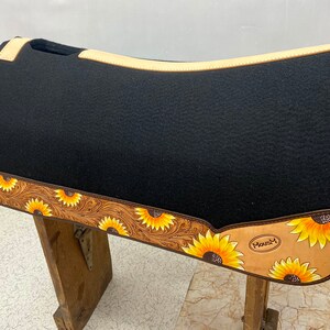May include: Black saddle pad with a tan leather border and sunflower design. The border is tooled with a floral pattern. The saddle pad has the word "Mousy" printed on it.