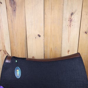 May include: Black saddle pad with brown leather trim and a green and yellow label that says "Horseware".