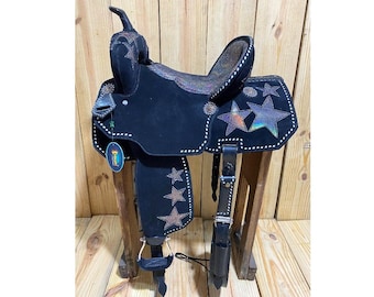 May include: Black leather saddle with a silver and iridescent star design. The saddle is on a wooden stand.