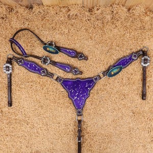 May include: Purple and silver horse tack set with a leather headstall, breast collar, and reins. The set is decorated with rhinestones and a silver concho.