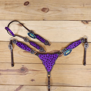 May include: Purple and brown leather horse bridle with a leopard print design. The bridle has silver conchos and rhinestones.