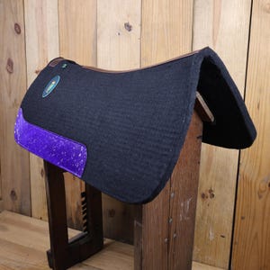 May include: Black saddle pad with a purple and white patterned trim. The saddle pad is made of a thick, soft material and is designed to protect the horse's back.