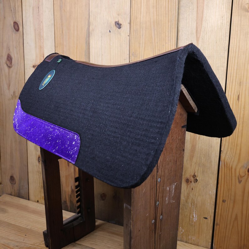 May include: Black saddle pad with a purple and white patterned trim. The saddle pad is made of a thick, soft material and is designed to protect the horse's back.