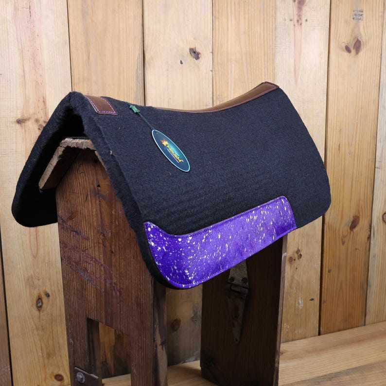 May include: Black saddle pad with a purple and white speckled trim. The saddle pad has a brown leather binding and a green tag that says "Professional's Choice".