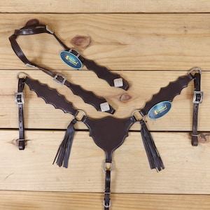 Könnte beinhalten: Ein braunes Leder-Pferdezaum-Set mit silberfarbenen Schnallen und dekorativen Akzenten. Das Set beinhaltet einen Kopfriemen, einen Stirnriemen und einen Brustriemen mit einem wellenförmigen Randdesign. Enthält eine Brustplatte mit Quasten und einem Mittelriemen.