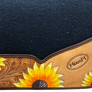May include: A black felt saddle pad with a brown leather border and sunflower design. The leather is tooled with a floral pattern and the brand "Yousi" is embossed in the lower right corner.