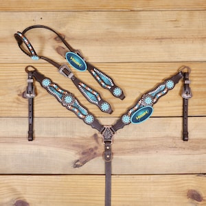 Puede incluir: Un conjunto de guarnicionería para caballos en cuero marrón oscuro que incluye una cabezada y un petral. Ambas piezas presentan incrustaciones de color turquesa, conchos plateados en forma de flor y costuras blancas. Etiqueta azul HOUSH.
