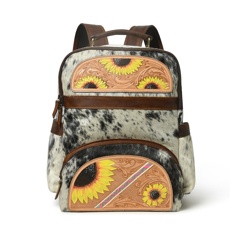 May include: A brown leather backpack with a white and black cowhide pattern. The backpack has a large front pocket with a tooled leather design featuring three yellow sunflowers. The backpack also has a smaller front pocket with a tooled leather design featuring two yellow sunflowers.