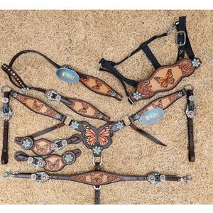 May include: A brown leather horse tack set featuring embossed butterfly patterns, turquoise-colored floral conchos, and silver-toned hardware. The set includes a headstall, a breast collar, and matching spur straps, all decorated with detailed butterfly motifs.