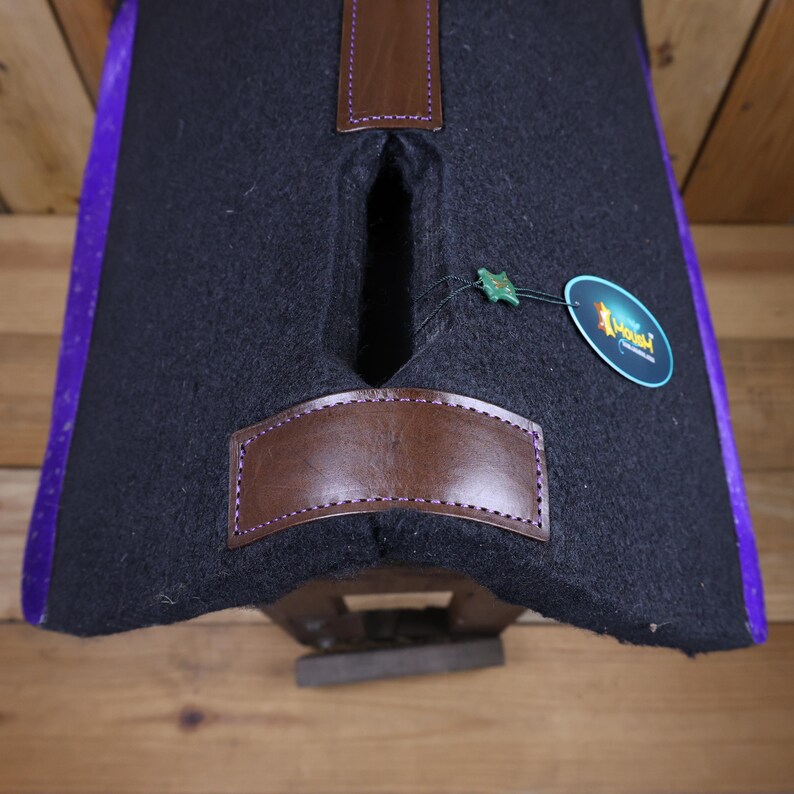 May include: Black saddle pad with purple trim and a brown leather patch. The saddle pad has a cutout for the saddle horn and a small green star tag.
