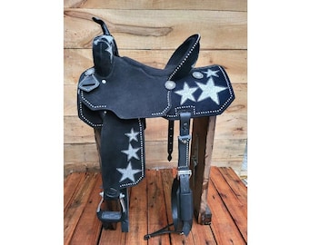 May include: A black western saddle featuring silver glitter star appliques on the seat, fenders, and skirts. The saddle is accented with silver studs along the edges and includes a horn, a high cantle, and metal stirrups with black tread.