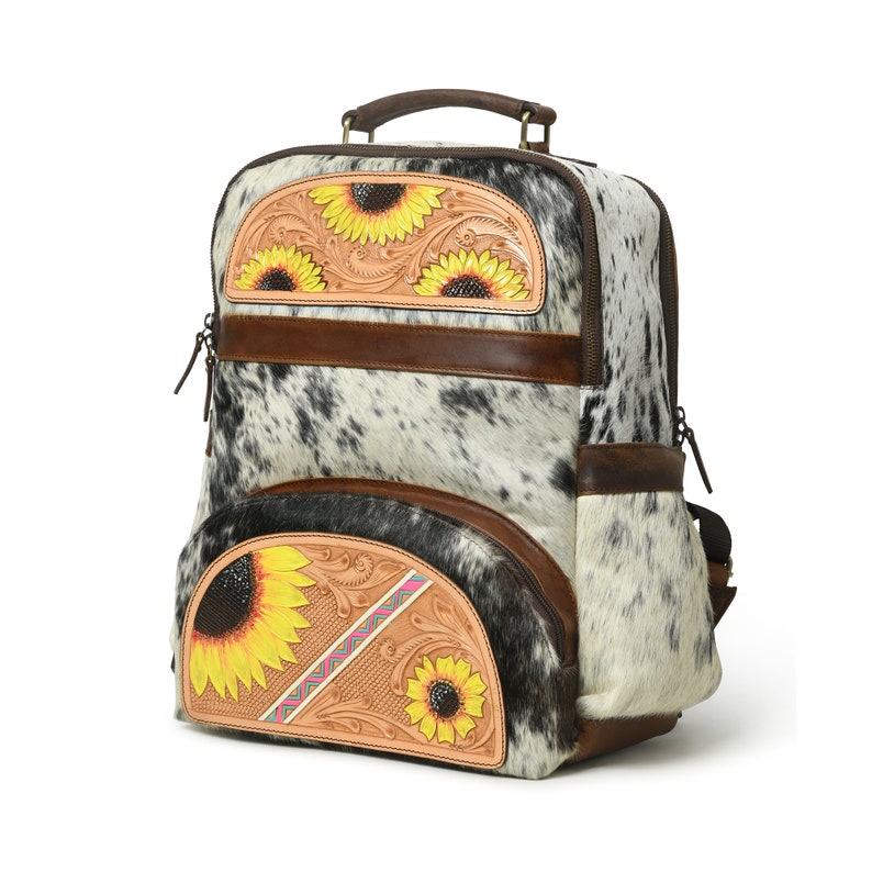 May include: A brown leather backpack with a white and black cowhide pattern. The backpack has two large pockets with sunflower embroidery and a smaller pocket on the front. The backpack has a brown leather handle and adjustable straps.