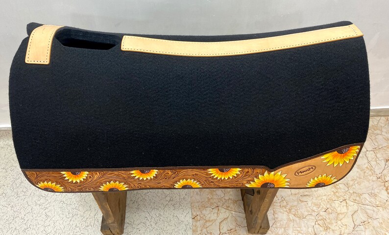 May include: Black saddle pad with a tan leather border and sunflower design. The saddle pad has a cutout for the saddle horn and the text "Manny's" is visible on the bottom right corner.