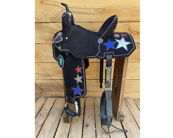 May include: Black leather saddle with a star design featuring red, white, and blue rhinestones. The saddle is decorated with silver studs and has a black leather stirrup.