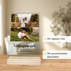 May include: A clear acrylic photo display with two images of a couple, set on a light wood base. The words "Lieblingsmensch, Julia und Marvin" are printed on the front. The display also has text that says "Mit eigenem Foto" and "Mit personalisiertem Wunschtext".