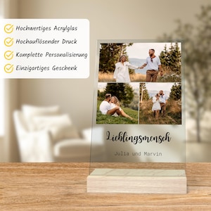 May include: A clear acrylic photo display with three images of a couple. The display has a wooden base and features the German word "Lieblingsmensch" and the names "Julia und Marvin". The top left corner has text in German.