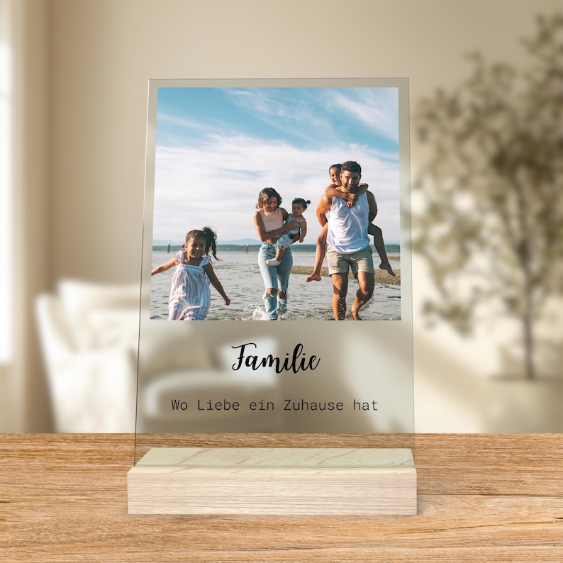 May include: A clear acrylic photo display featuring a family photo. The photo shows a family at the beach. The display has the word "Familie" and the phrase "Wo Liebe ein Zuhause hat" printed on it. The display sits on a wooden base.