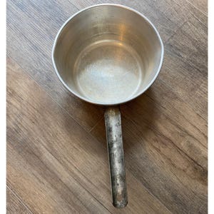 May include: A vintage, silver-colored saucepan with a long, sturdy handle. The pan has a rounded shape and a simple design, perfect for cooking. The handle is attached to the side of the pan and is made of the same metal.