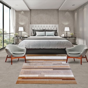 May include: A bedroom with a large bed, two gray chairs, and a brown and white striped rug. The bed has a white headboard with tufted buttons and a white duvet cover. The chairs are upholstered in a soft gray fabric and have wooden legs. The rug is made of a variety of materials, including leather and wool.