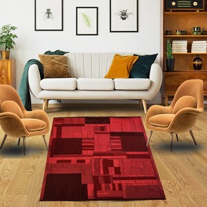 May include: A red and burgundy geometric patterned area rug with a modern design. The rug is in a living room setting with a white sofa and two orange armchairs.
