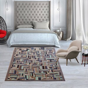 May include: A modern bedroom with a large upholstered headboard, a light blue bedspread, a beige armchair, and a geometric patterned rug in shades of brown, beige, and green.