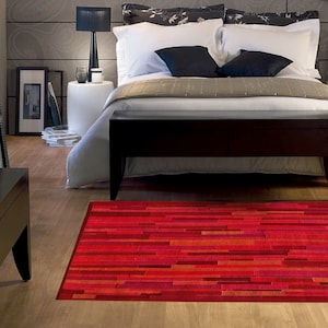 May include: A red and orange striped area rug with a modern design. The rug is in a bedroom with a bed and a wooden bench.