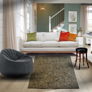 May include: A living room with a white sofa, a gray beanbag chair, a brown and black stool, and a rug with a brown and beige pattern. The room has white walls and a wooden floor.