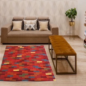 May include: A red, blue, and yellow patterned rug with a brown couch and a gold metal bench in front of a white wall with a diamond pattern.