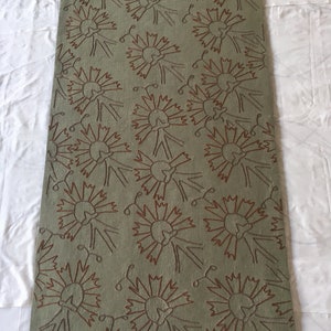 May include: A green rug with a repeating pattern of brown stylized flowers. The flowers have a circular shape with multiple petals and a stem with a curl at the end.
