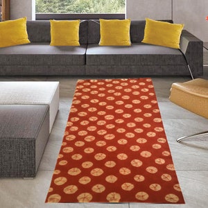 May include: A red and cream runner rug with a circular pattern. The rug is placed in a living room setting with a gray sofa and a brown armchair.