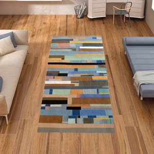May include: A colorful abstract area rug with a geometric pattern in shades of blue, green, yellow, and brown. The rug is laid out on a wooden floor in a living room setting.