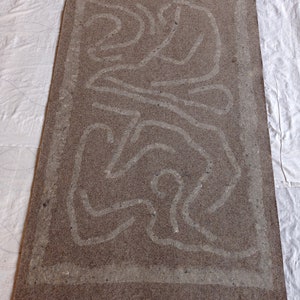 May include: A brown rug with a white border and a white abstract design. The design is made up of wavy lines and curves.
