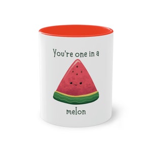 Op de afbeelding: Witte keramische mok met een rode rand. De mok heeft een watermeloenillustratie en de tekst "You're one in a melon".