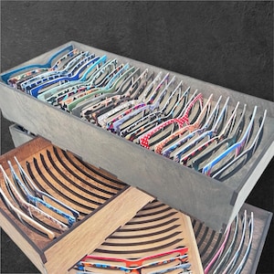 以下が含まれることがあります： 水玉模様、アニマルプリント、ストライプなど、さまざまな柄のフレームの眼鏡が木製のトレイに並べられています。トレイはさまざまなサイズと色で、さまざまな眼鏡のスタイルを紹介しています。