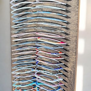 Peut inclure: Une collection de montures de lunettes colorées exposées sur une planche de bois. Les montures présentent divers motifs et couleurs, notamment des styles bleus, roses et à motifs. La planche de bois a une surface texturée avec des rainures.