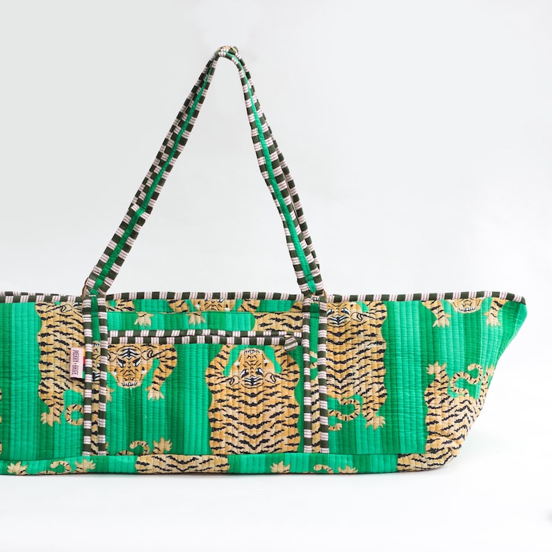 Puede incluir: Un bolso tote verde con estampado de tigre. La bolsa presenta un dise&ntilde;o acolchado con rayas verticales y un patr&oacute;n repetido de tigres en tonos marrones y negros. Las asas son a rayas en negro, blanco y verde.