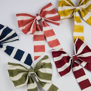 May include: Five striped fabric bows in different colours: red, yellow, blue, green, and burgundy. The bows are tied with white stripes.