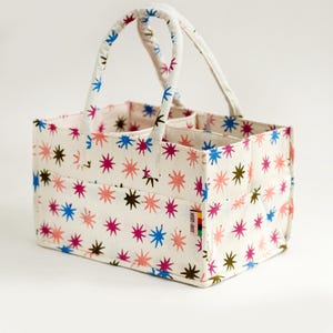 May include: A white canvas tote bag with a star pattern in pink, blue, and brown. The bag has two handles and a label that says "NORTH STREET".