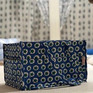 Peut inclure: Un sac fourre-tout rectangulaire en tissu avec un motif répétitif d'étoiles vert foncé centrées dans des cercles blancs sur fond bleu. Le sac comprend deux anses en tissu, plusieurs poches extérieures et une petite étiquette rectangulaire Heart Brute.