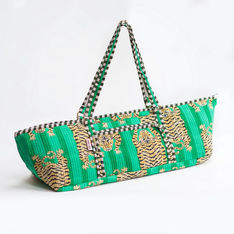Puede incluir: Bolso tote verde con estampado de tigre dorado y negro. El bolso tiene forma rectangular con cierre de cremallera y dos asas. Las asas y el ribete presentan un estampado de cuadros blancos y negros.