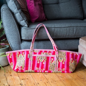 Puede incluir: Bolso tote rectangular con rayas rosas y rojas y un estampado de tigre repetido. El estampado de tigre es en oro y negro. El bolso tiene dos asas y est&aacute; sobre un suelo de madera.