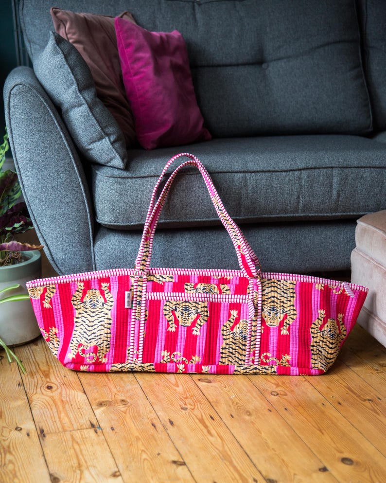 Puede incluir: Bolso tote rectangular con rayas rosas y rojas y un estampado de tigre repetido. El estampado de tigre es en oro y negro. El bolso tiene dos asas y est&aacute; sobre un suelo de madera.