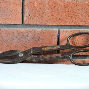 May include: A vintage, rusty, metal snips with a black handle and a gold label that reads "DROP FORGED".