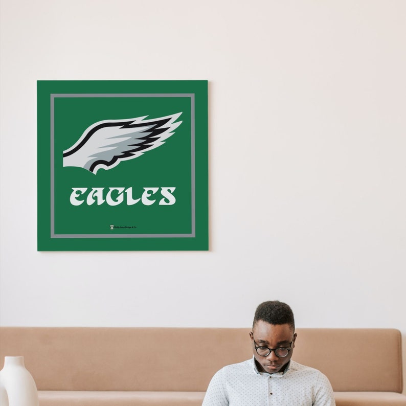 May include: A green square with a white and black eagle wing graphic and the word "EAGLES" in white text. The square is framed with a grey border.